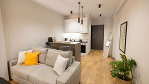 Ett modernt vardagsrum med en soffa, en matplats med ett kök i bakgrunden och en hall som leder till en dörr.