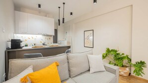 Ett modernt vardagsrum med en grå soffa, en kaffemaskin och en matplats med ett vitt skåp.