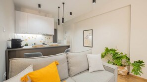 Een moderne woonkamer met een grijze bank, een koffieapparaat en een eethoek met een wit kastje.
