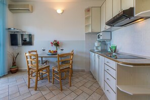 A compact kitchen with a dining table, chairs, a TV mounted on the wall, and a microwave. - Beautiful apartment in a quiet residential area in Crikvenica (Crikvenica)