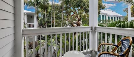 A covered porch with white railings, a round table, and two wicker chairs.