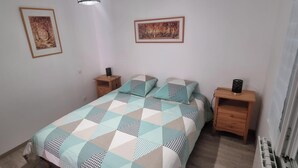 Quarto com cama, duas mesas de cabeceira, um radiador e duas fotografias emolduradas na parede.