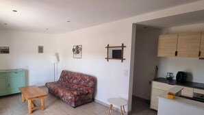 Uma sala de estar com sofá, uma mesa pequena, um armário e uma cozinha compacta.