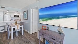 A room with a kitchen, dining area, and a large window with a beach view. - Island Sunrise 464 by Liquid Life (Gulf Shores)
