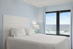 Ein Schlafzimmer mit Bett, Nachttisch, Lampe und Meerblick durch ein Fenster.