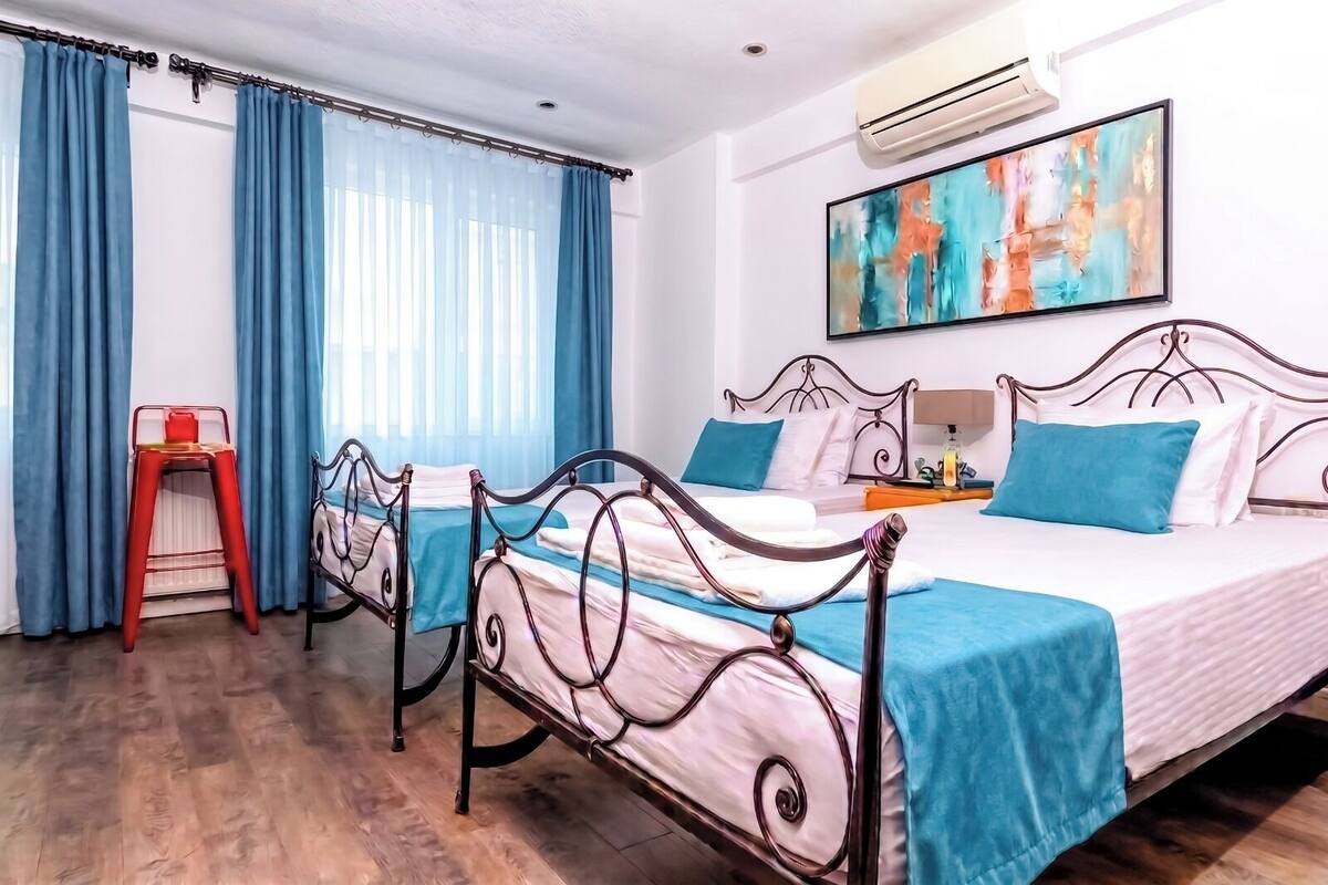 A hotel room with two beds, a red chair, a blue curtain, and a painting on the wall.