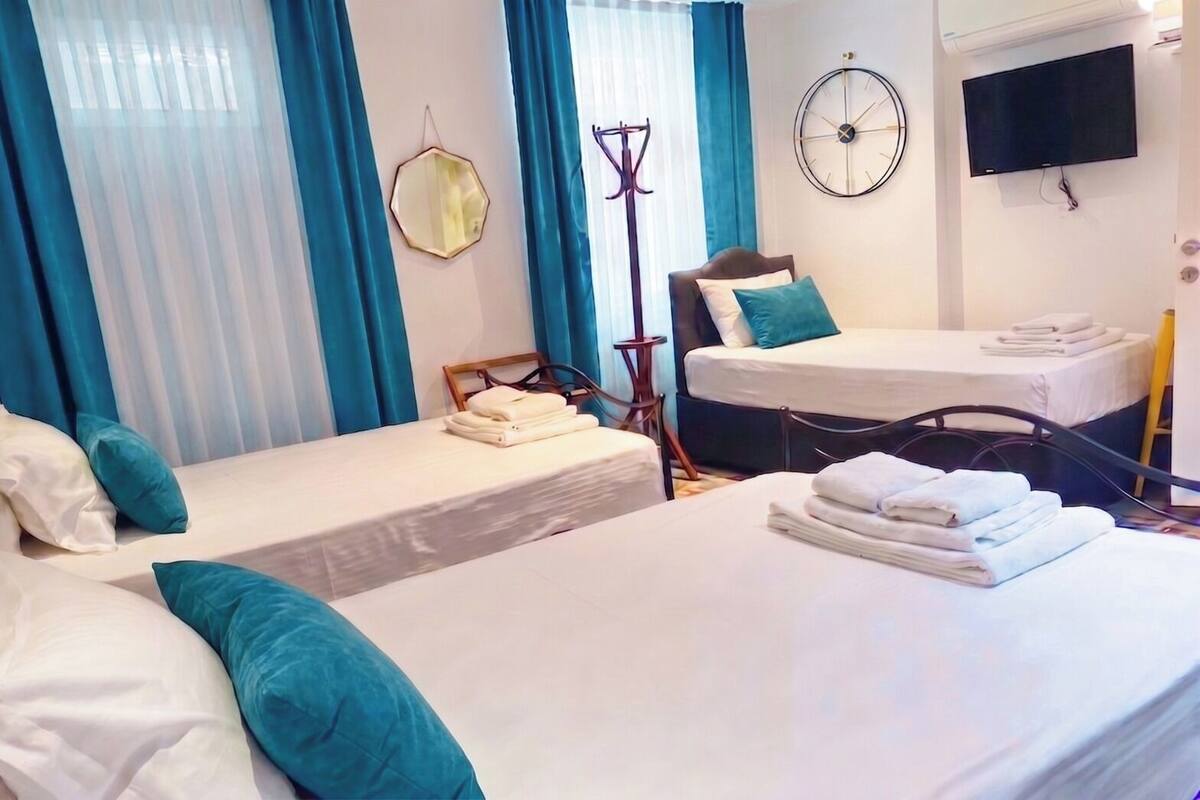 A hotel room with two beds, a clock, a TV, and a window with curtains.