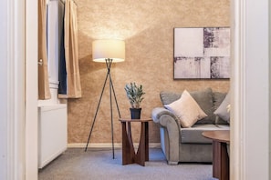 Un salon avec un canapé, une lampe, une petite table sur laquelle se trouve une plante, et un tableau accroché au mur.