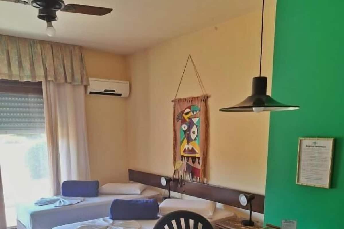 Una habitación de hotel con cama, mesa de comedor, una silla, ventilador de techo y pared verde.