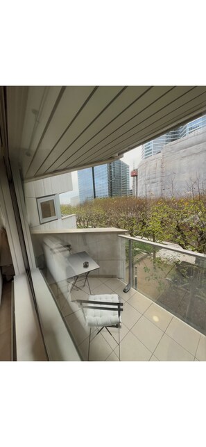 Ein moderner Balkon mit Glastrennwand, einem kleinen Tisch und einem gepolsterten Stuhl.