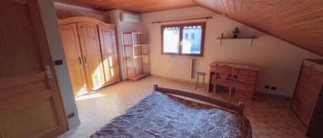 Un dormitorio con techo inclinado, armario de madera, cama, escritorio pequeño y ventana.