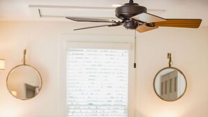 Ein Schlafzimmer mit einem Bett, Nachttischlampen, einem Deckenventilator und einem Fenster mit Jalousien.