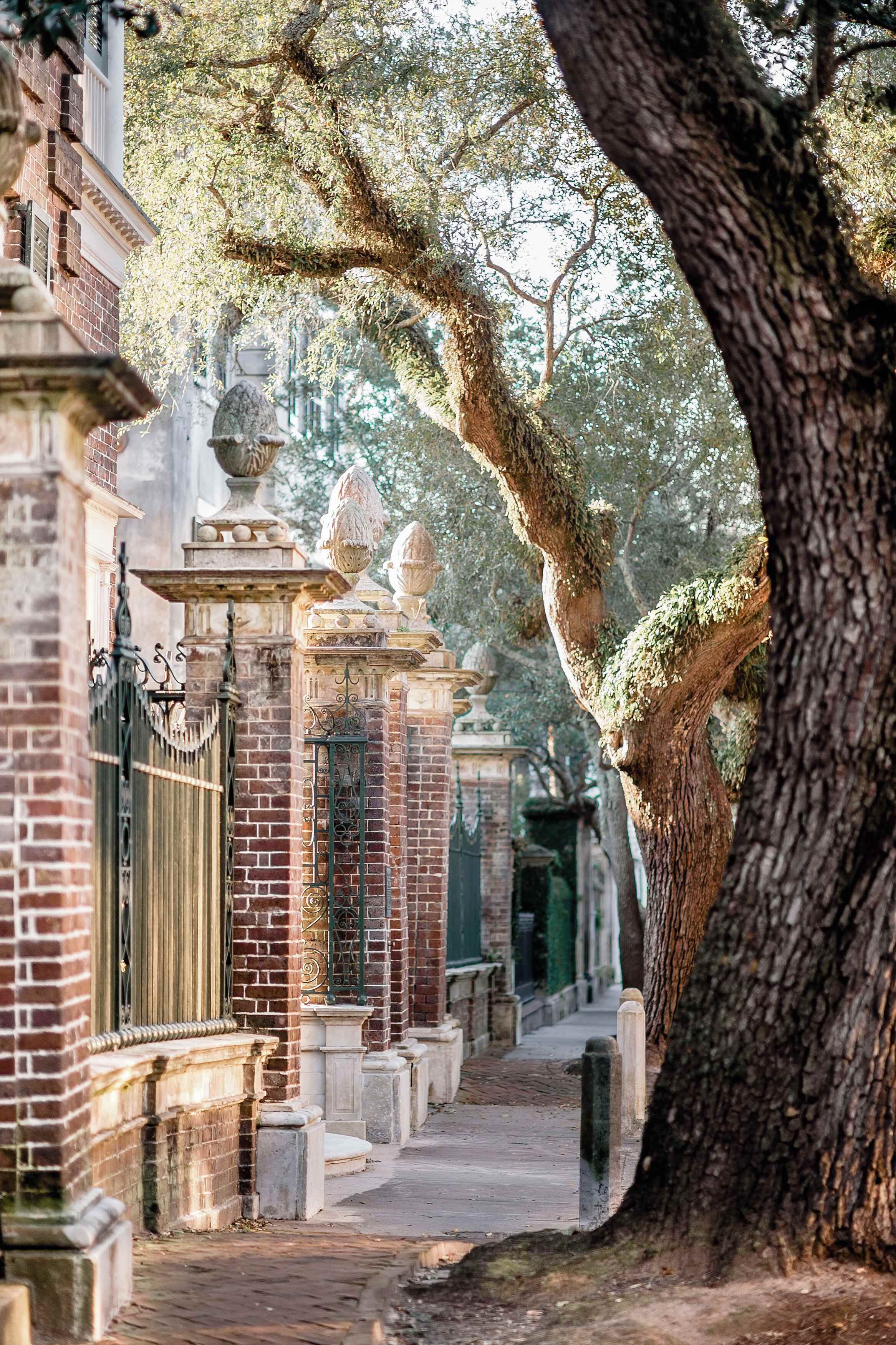 A pathway lined with brick buildings and stone pillars, leading to a gate.