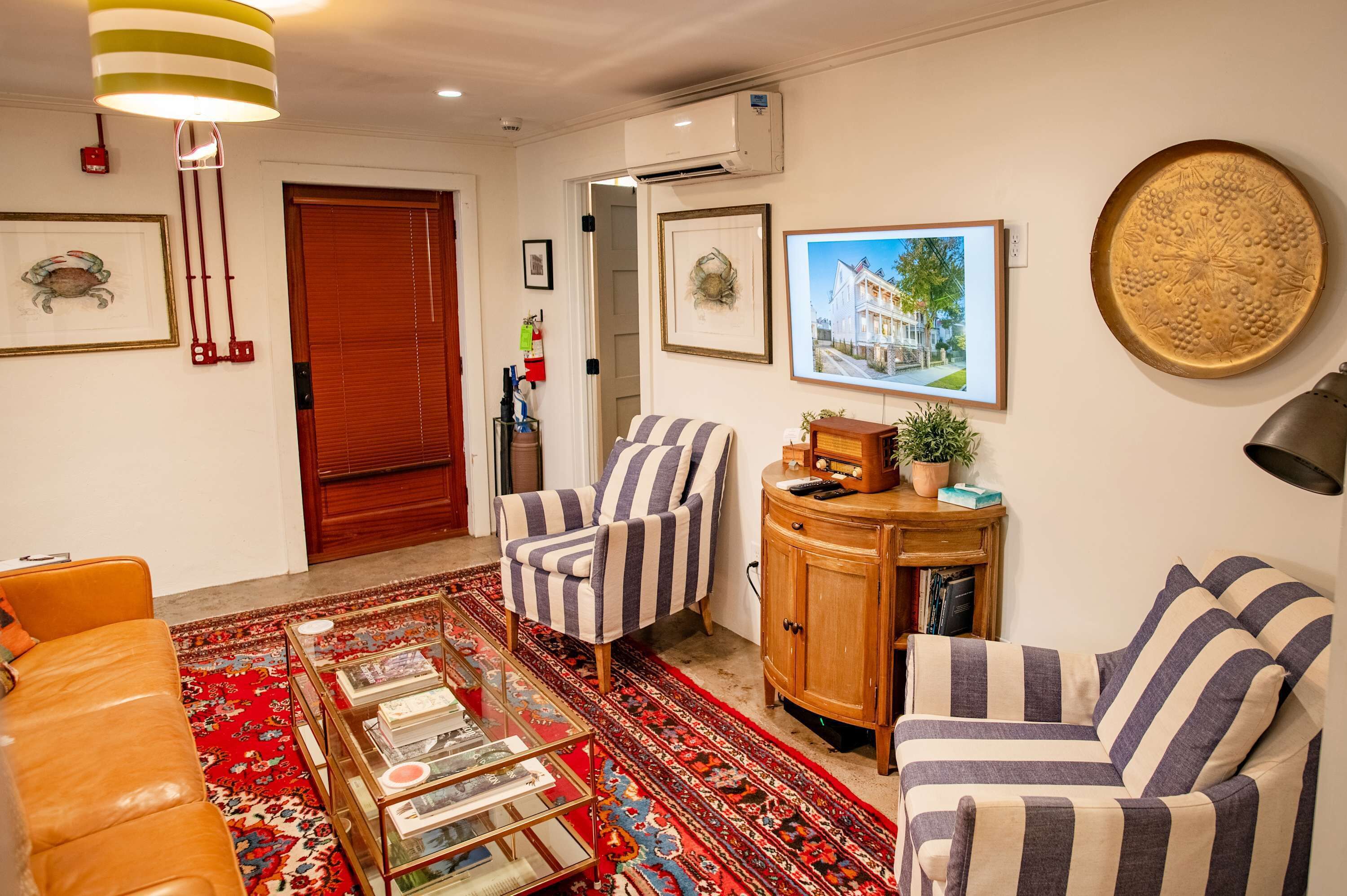 Una sala de estar con sillones a rayas, un tapete rojo estampado, una mesa de centro de cristal y un mueble de madera.