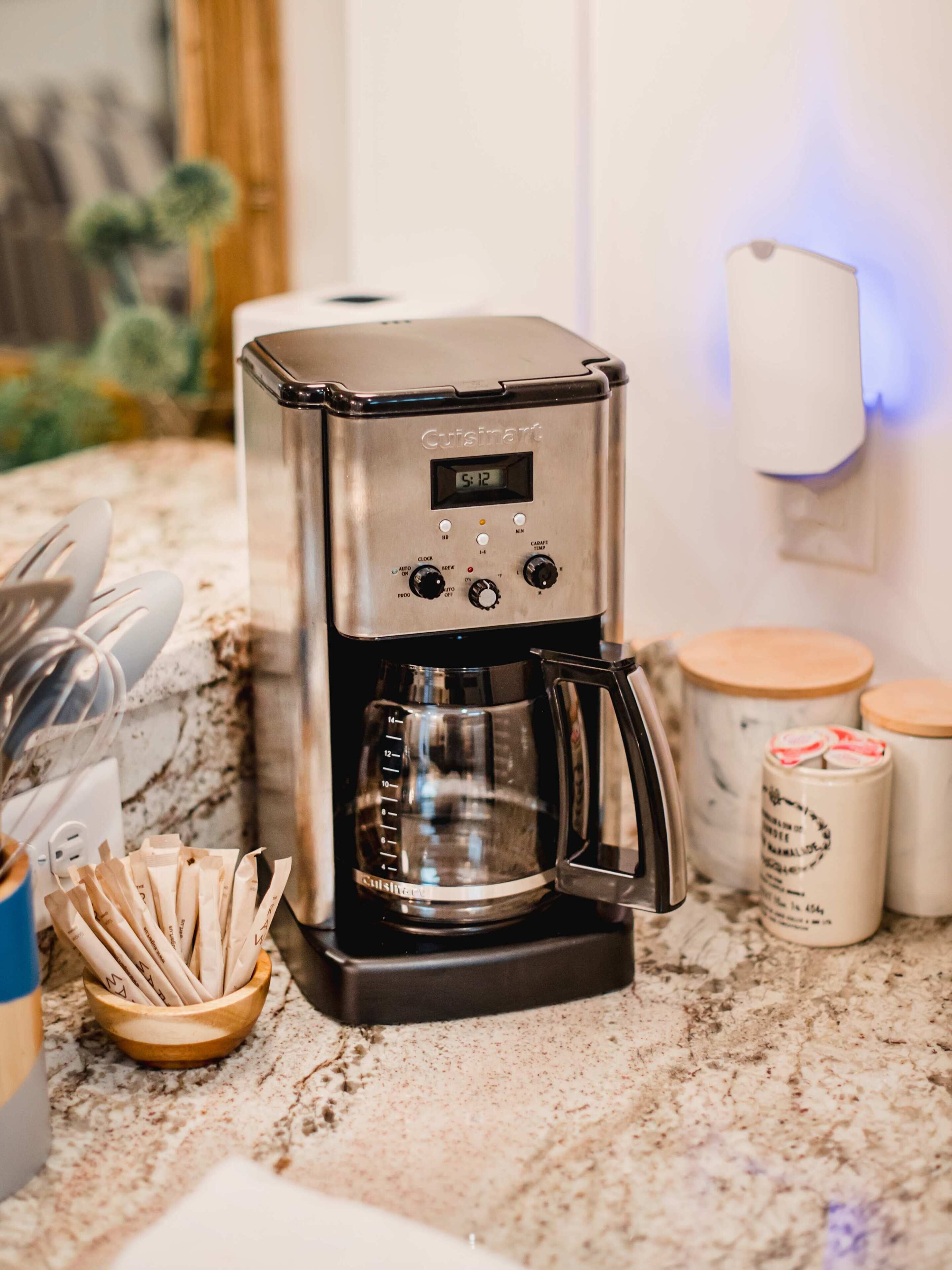 A kitchen with a coffee maker, a wooden bowl with utensils, and jars on the counter.