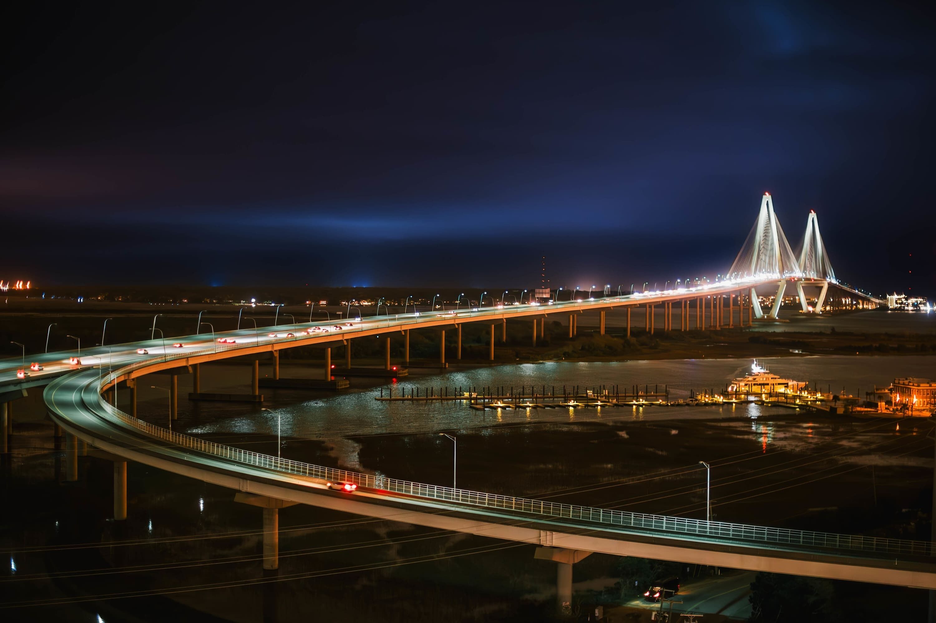 Vista noturna de uma grande ponte iluminada, com várias faixas e um rio abaixo.