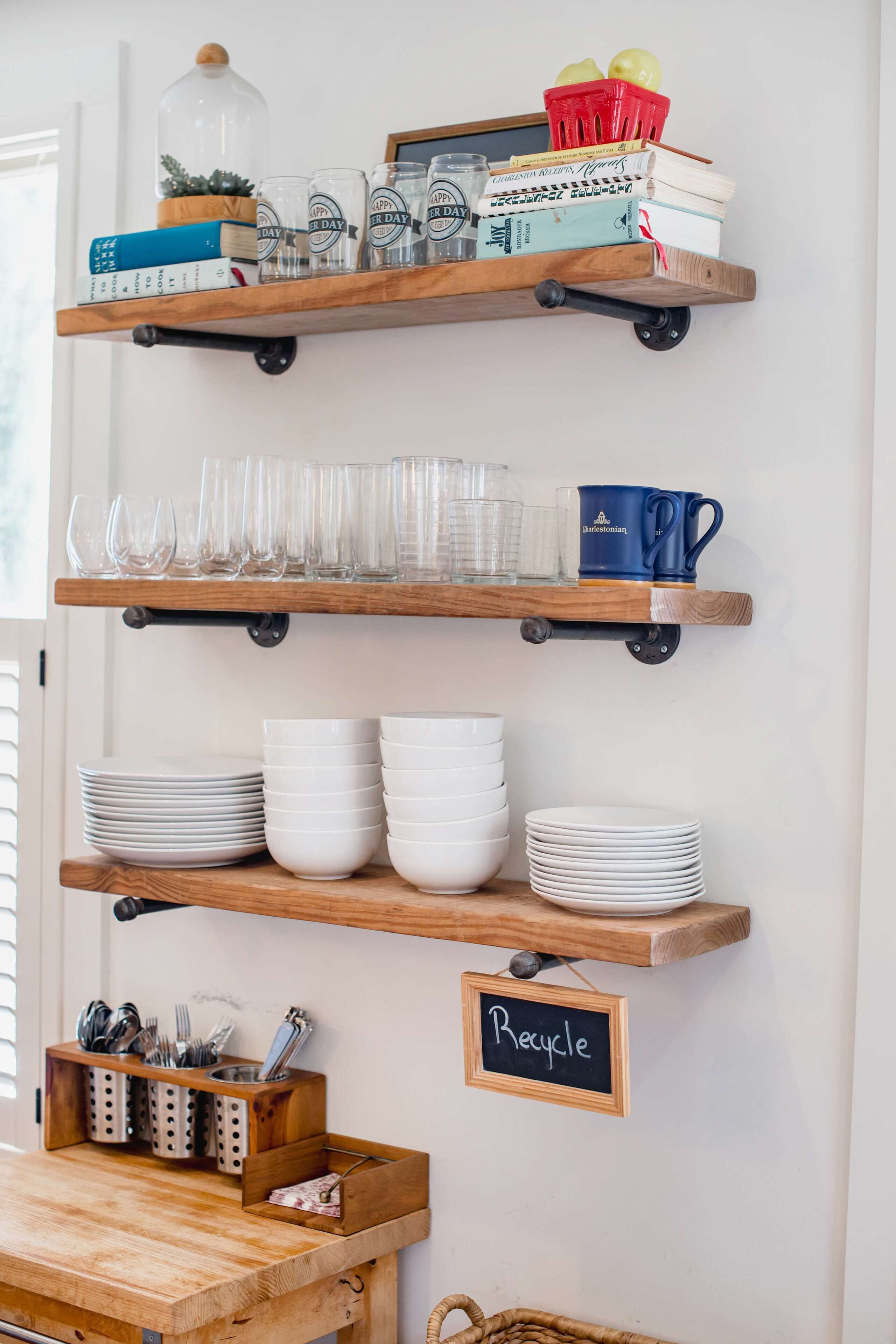 Una cocina con estantes de madera que sostienen cristalería, platos y un letrero que dice 'Recycle'.