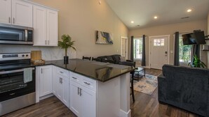 A kitchen with white cabinets, a microwave, an oven, and a dining area with a sofa and table. - Modern Upper Retreat w Free Tix Deck 2 Suites (Hendersonville)