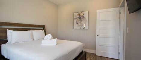 A bedroom with a bed, a white door, and a painting on the wall.