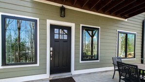 Une maison avec une porte d’entrée noire, deux fenêtres à cadres blancs et une terrasse avec une table et des chaises.