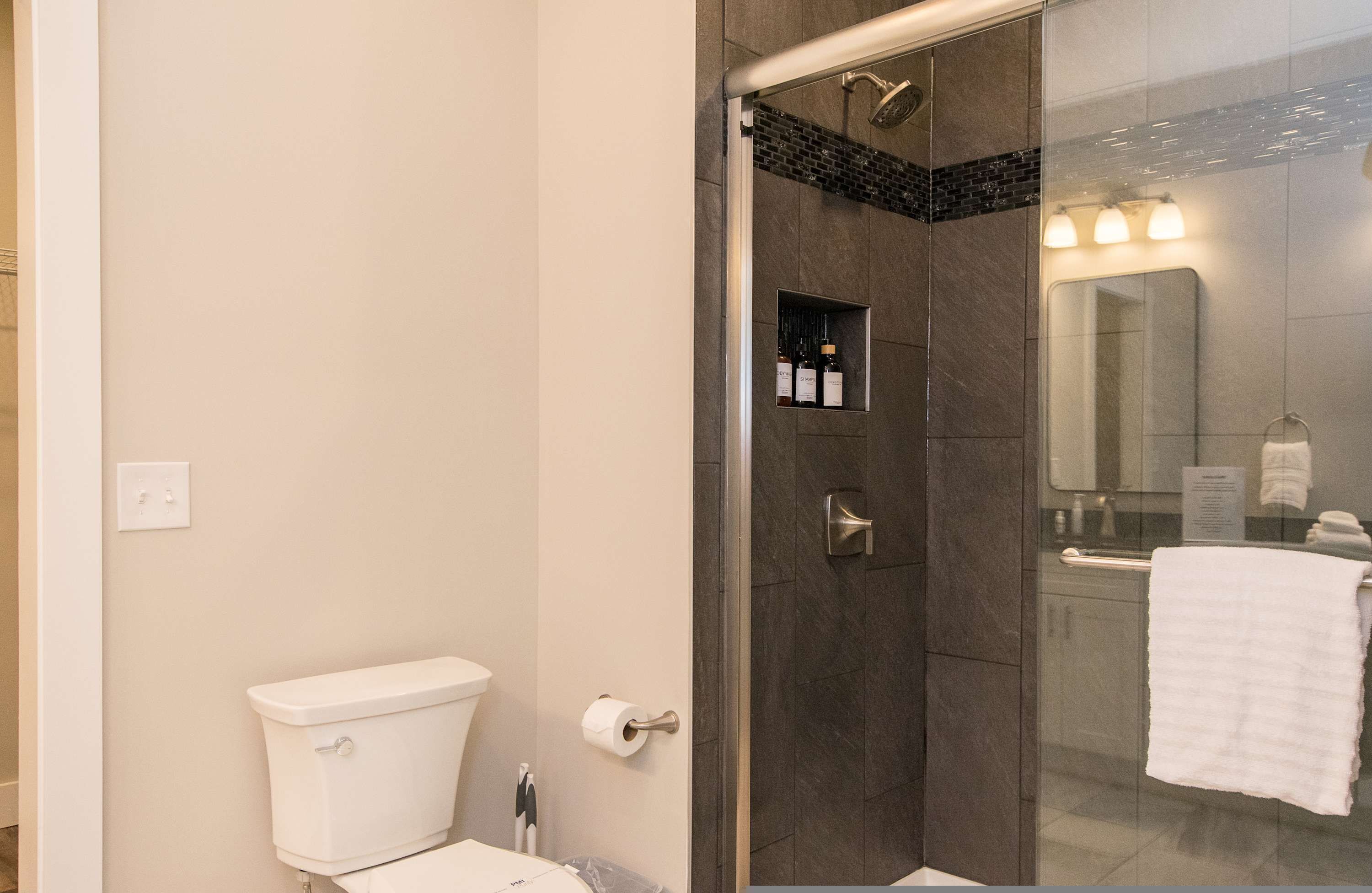 A modern bathroom with a glass-enclosed shower, a toilet, a sink, and a mirror.