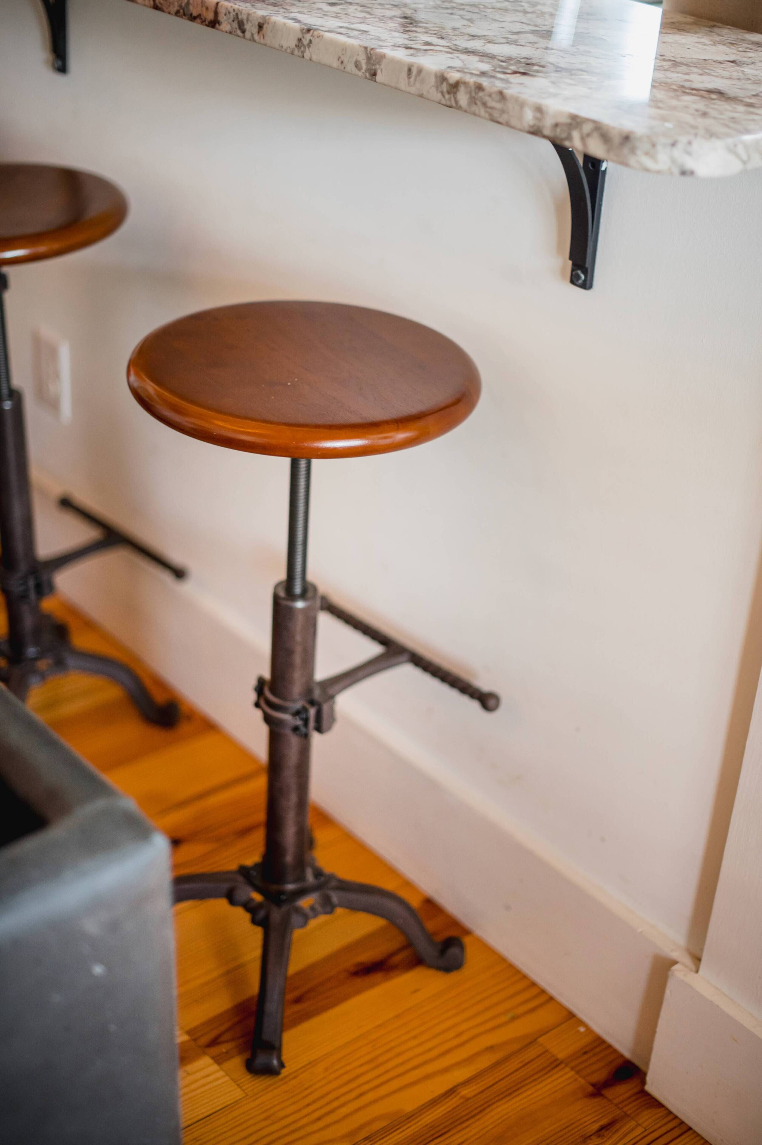 Une cuisine dotée d’un plan de travail en marbre, d’un tabouret en bois avec un pied en métal et d’un plancher en bois.