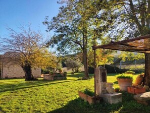 Un giardino con una pergola, elementi in pietra e piante in vaso.
