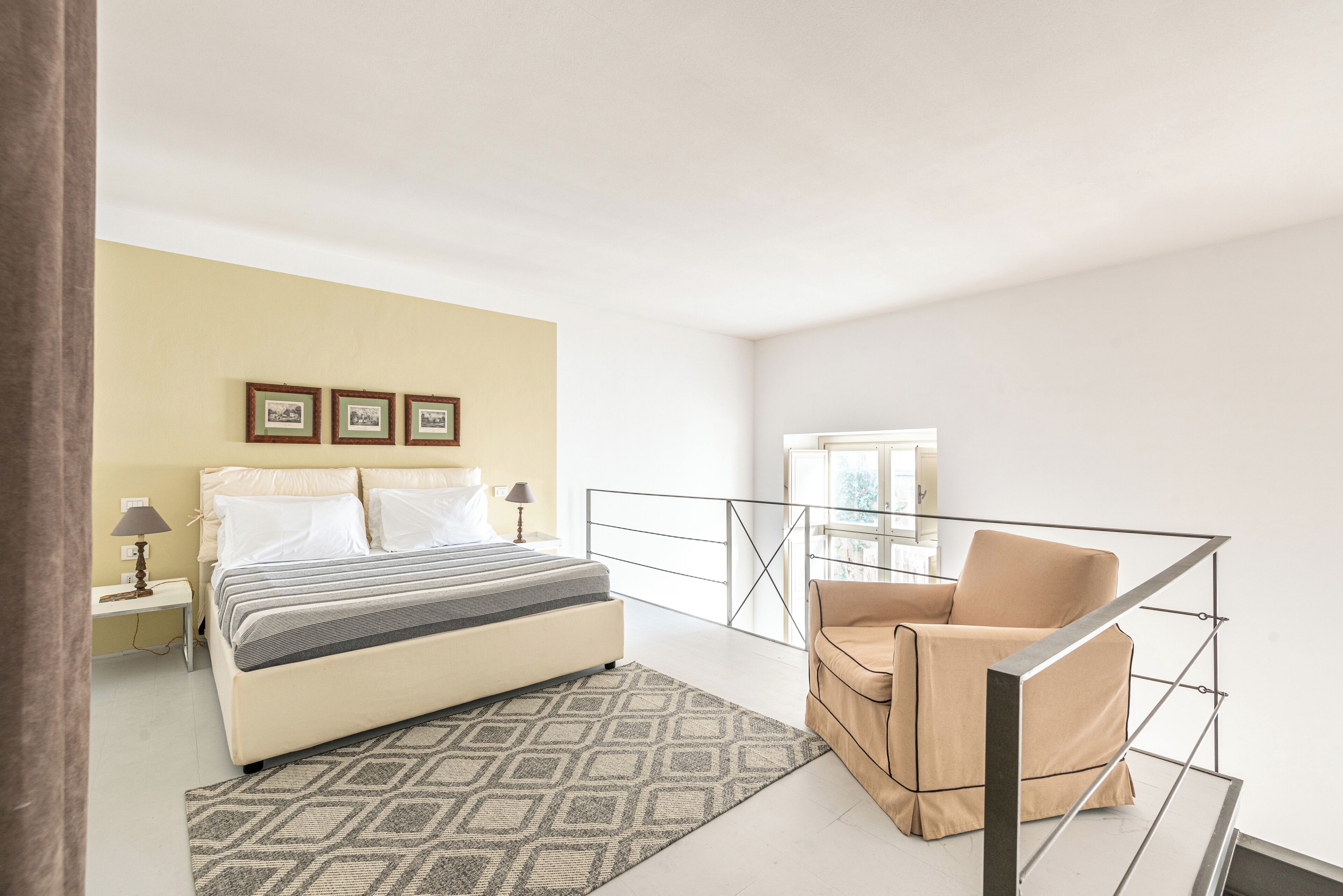 A bedroom with a bed, bedside table, lamp, and a chair with a metal railing.
