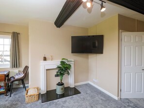 A room with a fireplace, a television mounted on the wall, a door, and a window with curtains. - 3 Woods Farm House (Chippenham)