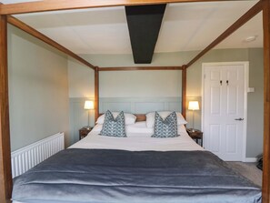 A four-poster bed with a dark grey bedspread, two bedside lamps, and a white door in a room with light green walls and wooden trim. - 3 Woods Farm House (Chippenham)