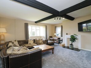 A living room with a leather sofa, a wooden coffee table, a fireplace, and a television mounted on the wall. - 3 Woods Farm House (Chippenham)