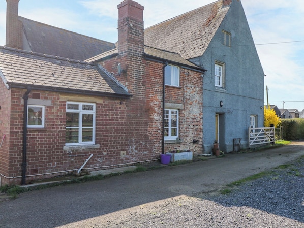 A traditional brick house with a sloped roof, a visible chimney, and a small garden area with a gate. - 3 Woods Farm House (Chippenham)