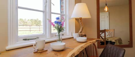 A wooden table with a lamp, a vase of flowers, and two white cups.