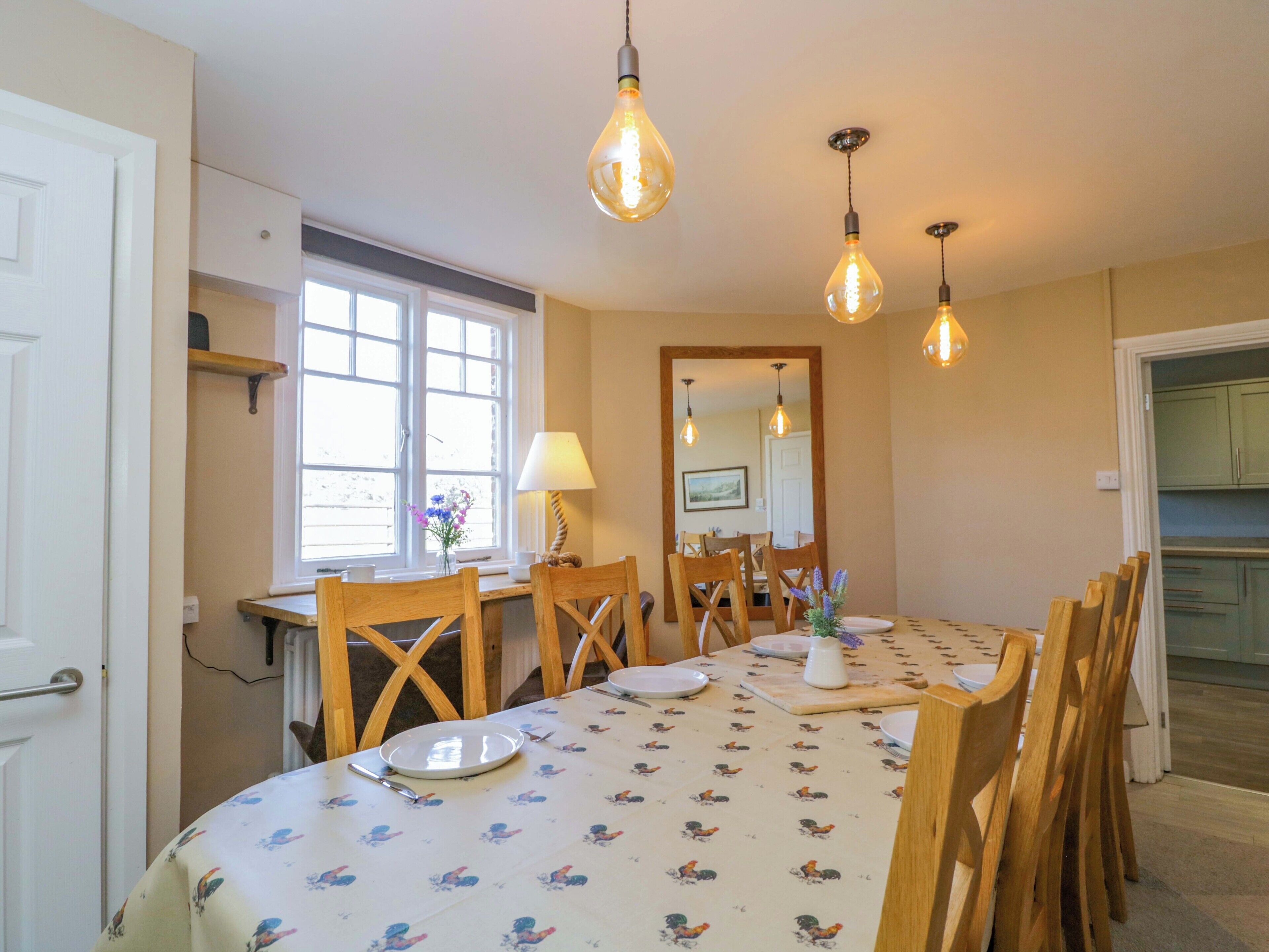 Un comedor con una mesa dispuesta para cuatro, sillas de madera, una ventana con luz natural y lámparas colgantes.