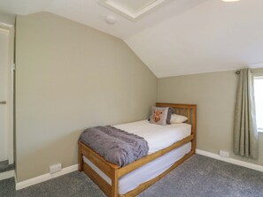 Un dormitorio con techo inclinado, una cama individual con cabecero de madera, alfombra gris y pared de color claro.