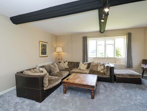 A living room with a sectional sofa, a wooden coffee table, a lamp, and a window with curtains. - 3 Woods Farm House (Chippenham)