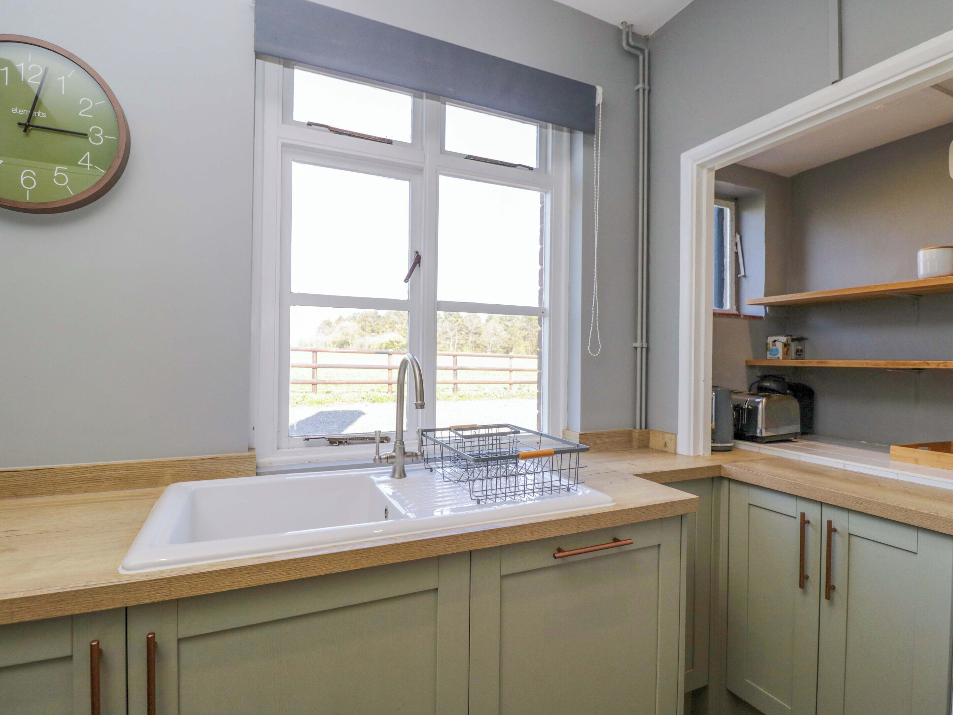 A kitchen with a window, a sink, a clock, and a toaster.