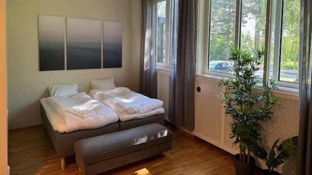 A bedroom with a bed, a bench, a large window, and a plant. - Söderåsen Airport Hotel (Ljungbyhed)