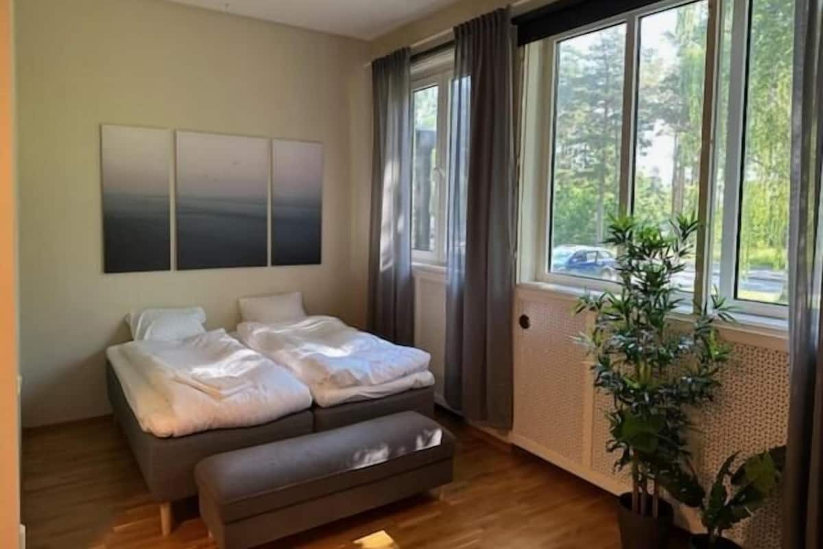 A bedroom with a bed, a bench, a large window, and a plant.