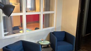 A room with two blue armchairs, a small round table, and a large window with curtains. - Söderåsen Airport Hotel (Ljungbyhed)