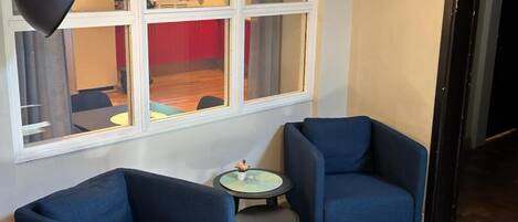 A room with two blue armchairs, a small round table, and a large window with curtains.