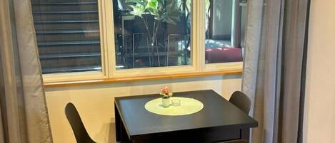 Una habitación con ventana, una mesa con dos sillas, una planta pequeña en maceta y una lámpara.