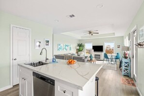 A modern kitchen with a dishwasher, a dining area with a TV, and a living room with a sofa and a TV.