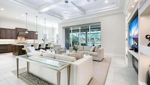 A modern kitchen with a large island, a dining area with a glass-top table, and a living room with a sofa set. - Luxury Naples Retreat / Pool, Near Beach (Naples)