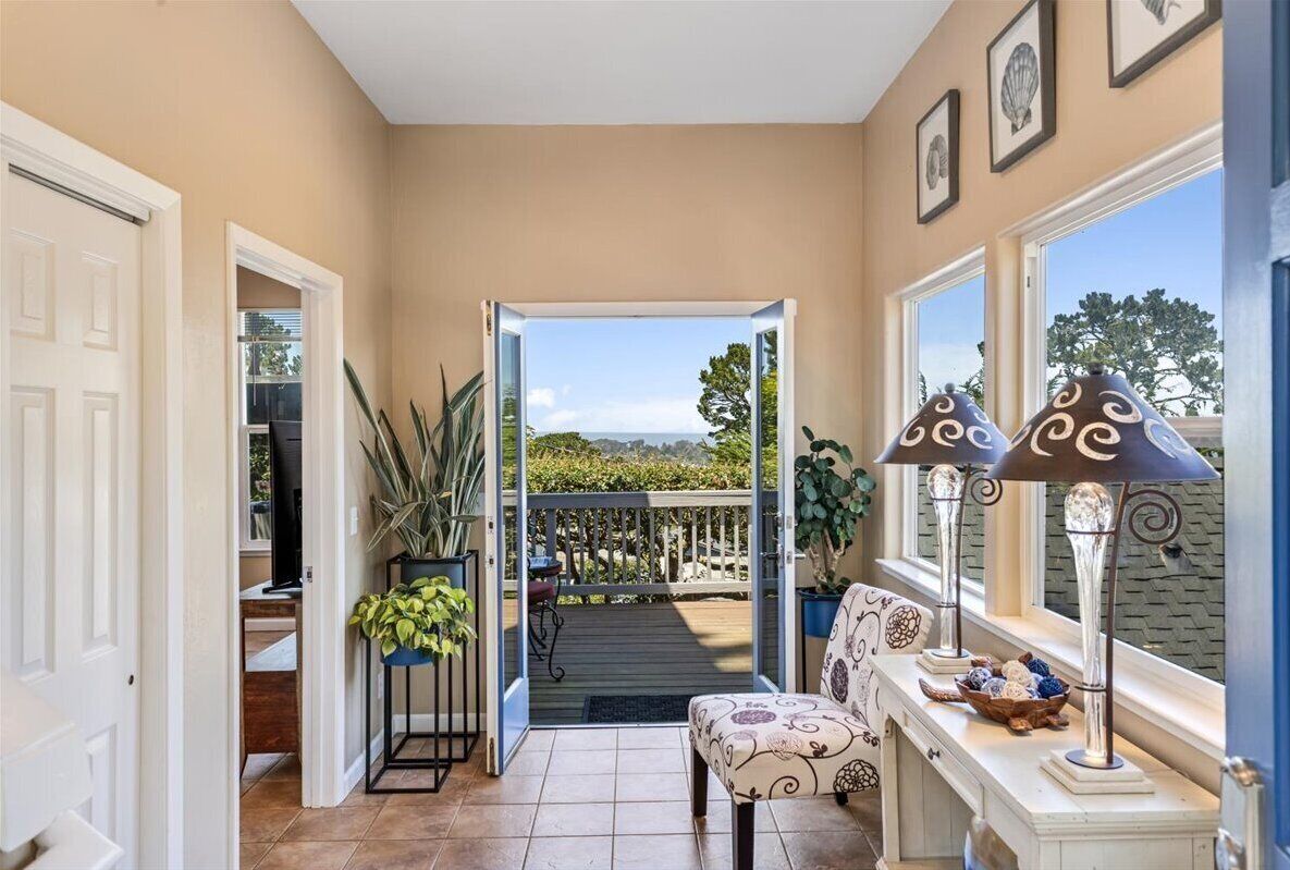 A hallway with a view of a deck, a potted plant, a lamp, and a chair.