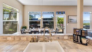 A kitchen with a sink, coffee maker, and dining area with outdoor seating. - 4073 Whale Watcher's Cove - Bay View Home (Monterey)