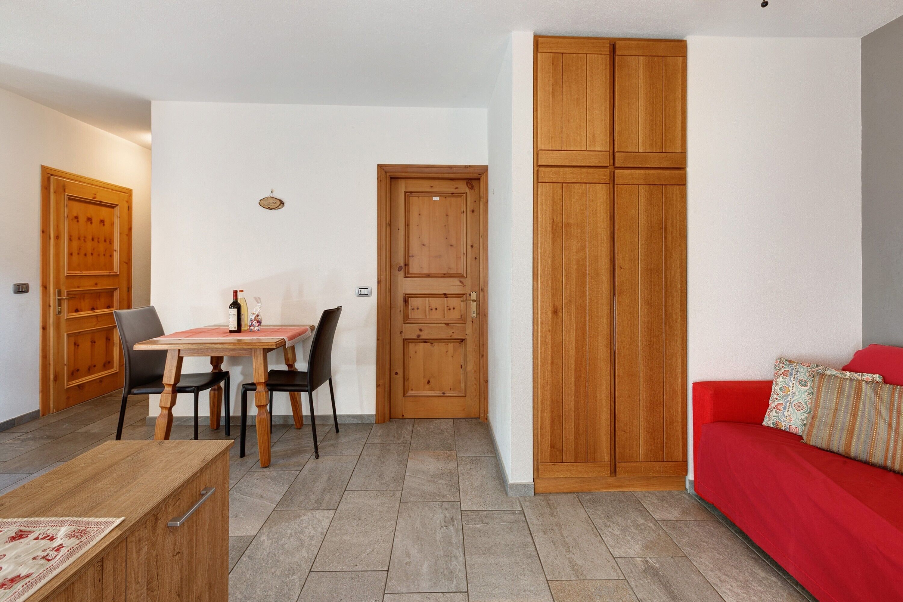 A room with a dining table, chairs, a red sofa, and wooden cabinets.