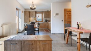 A modern kitchen with wooden cabinets, a dining area with a table and chairs, and a chandelier.