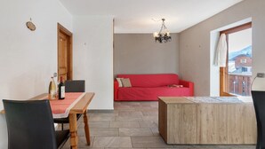 A room with a dining table, chairs, a red sofa, a wooden cabinet, and a chandelier.