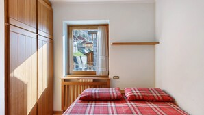 A bedroom with a window, wooden wardrobe, and a bed with plaid bedding.